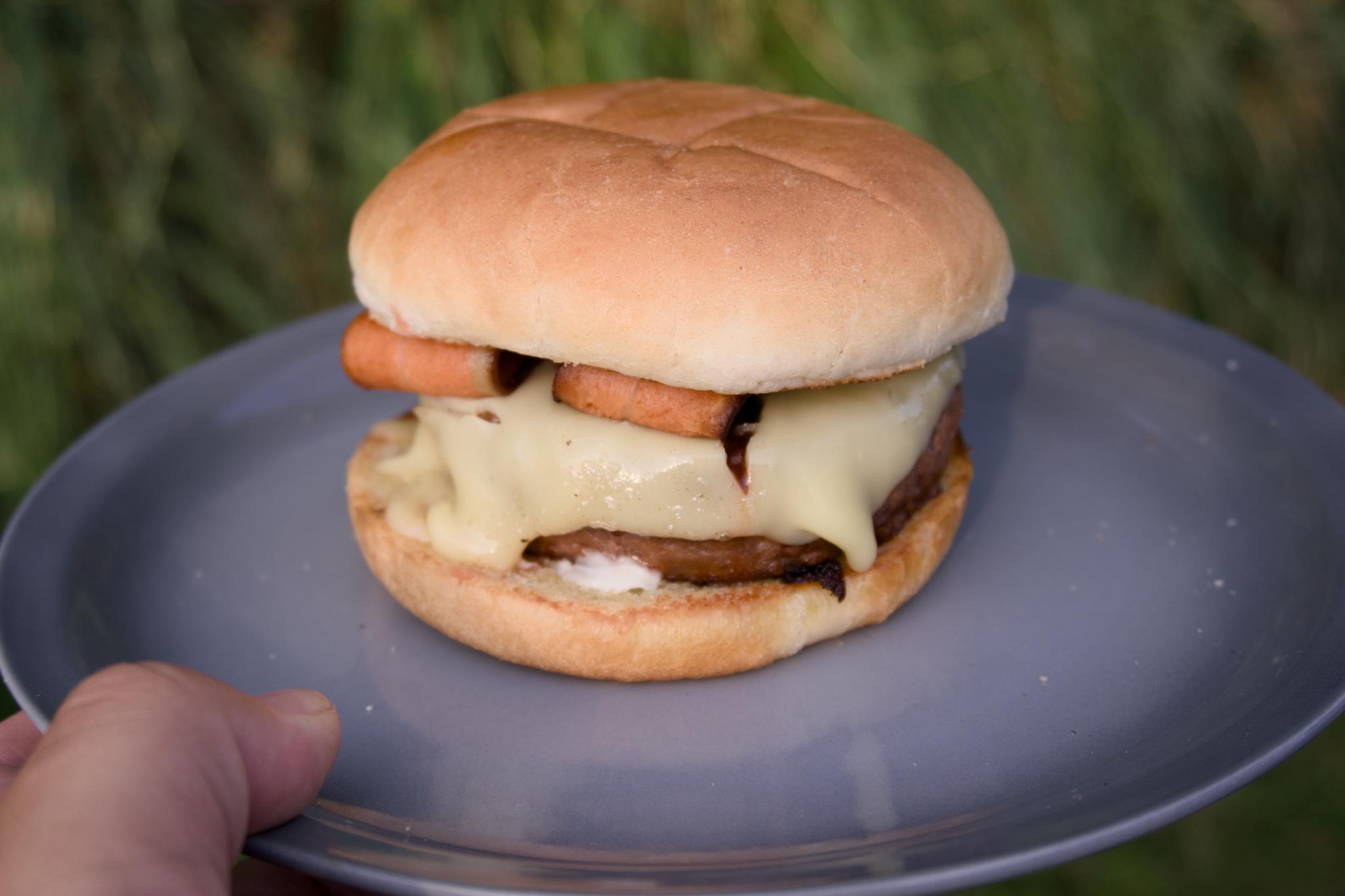 Burger with melted cheese and vegan bacon on a grey plate