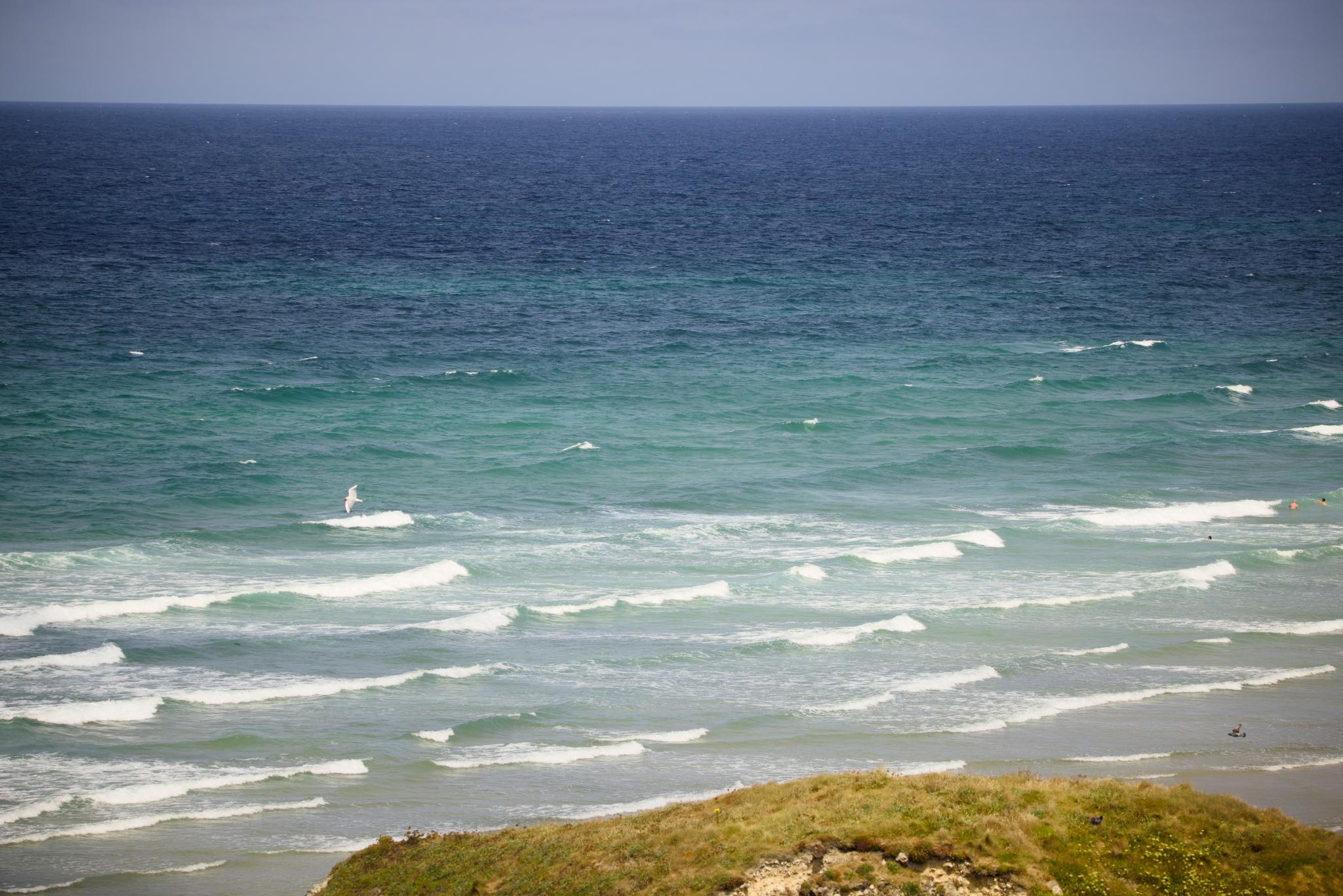 Lines of waves rolling in, swimmers in the water, headland in the foreground