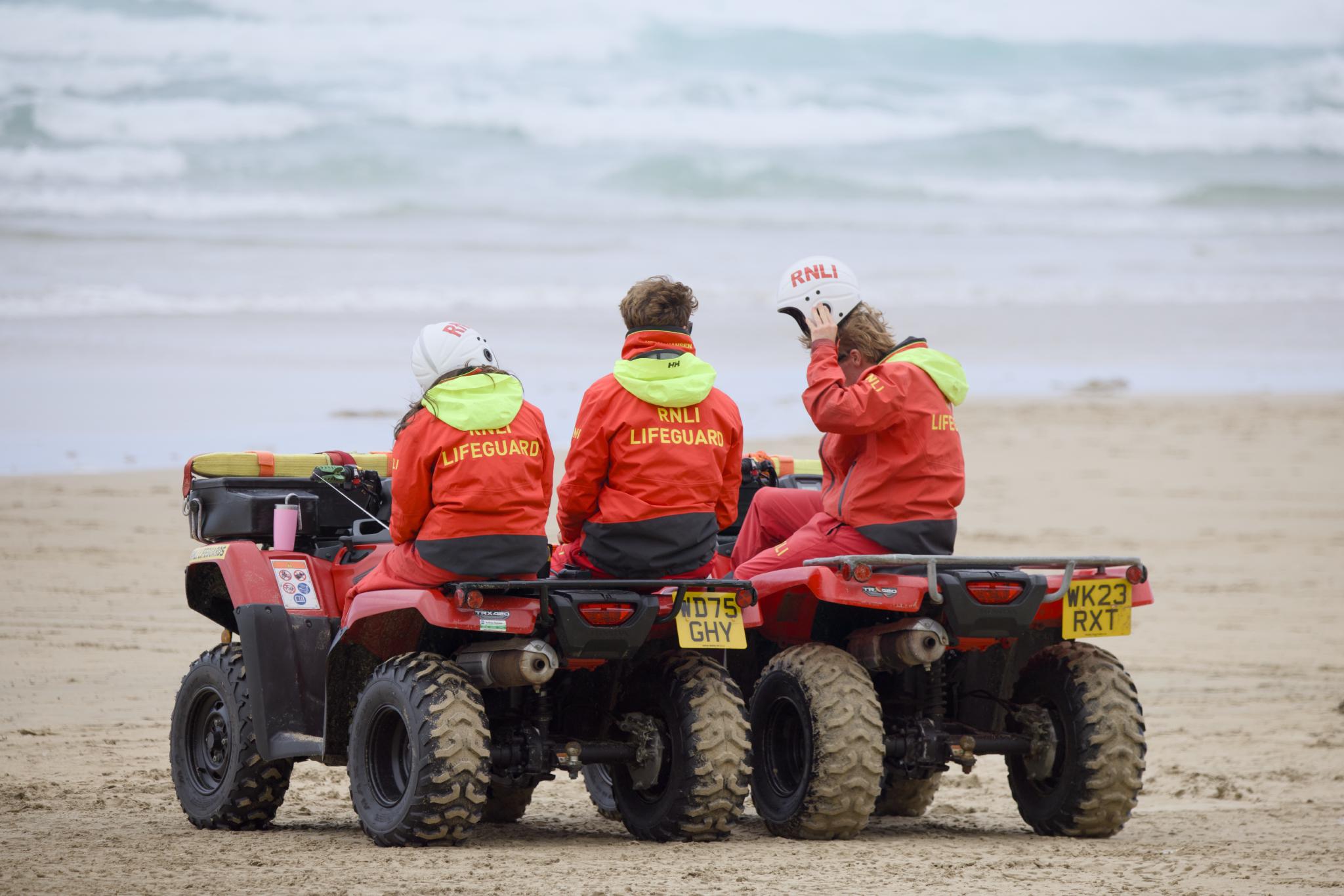 Three RNLI lifeguards on their quad bikes facing the sea