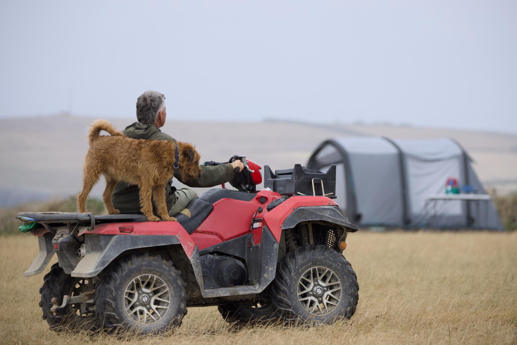 Farmer on a quad bike with a terrier standing on the back