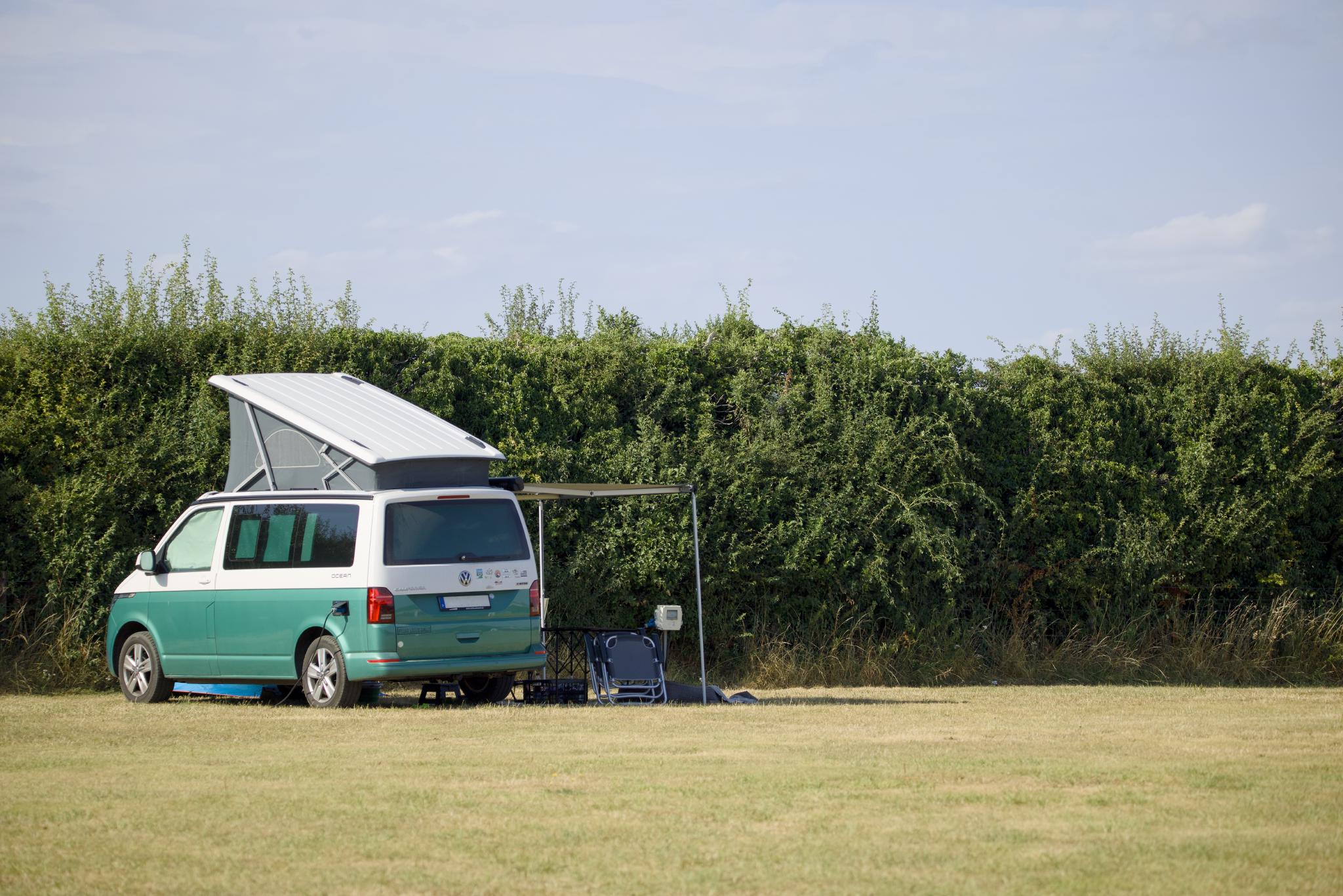 The California with the roof up and awning out on the pitch in front of a high hedge