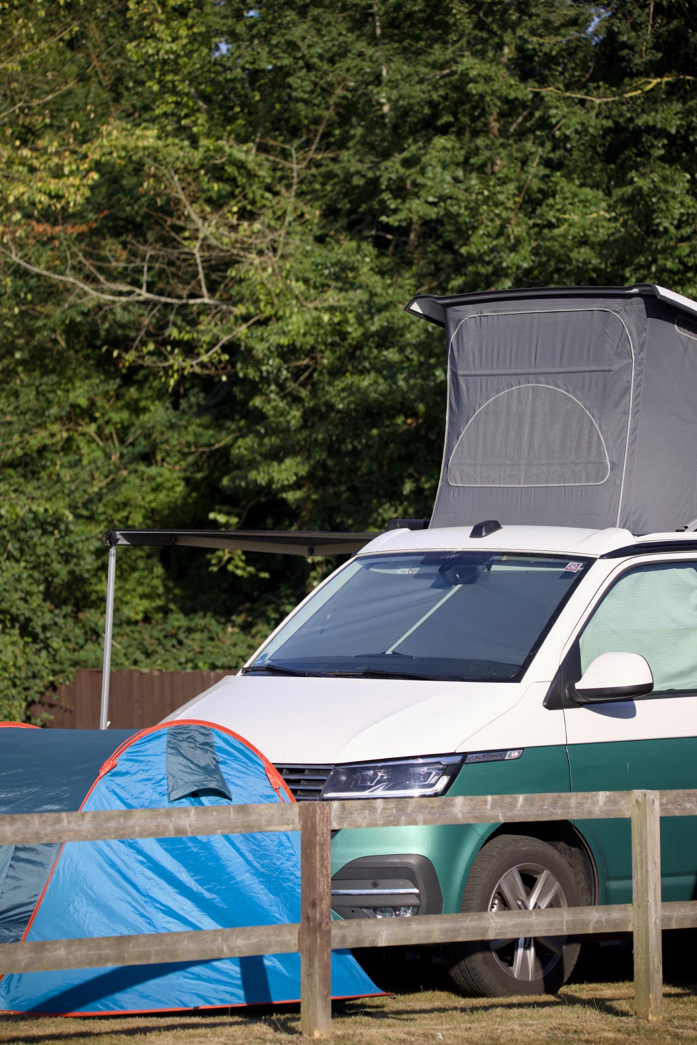 The California with the roof up and awning out behind a wooden fence