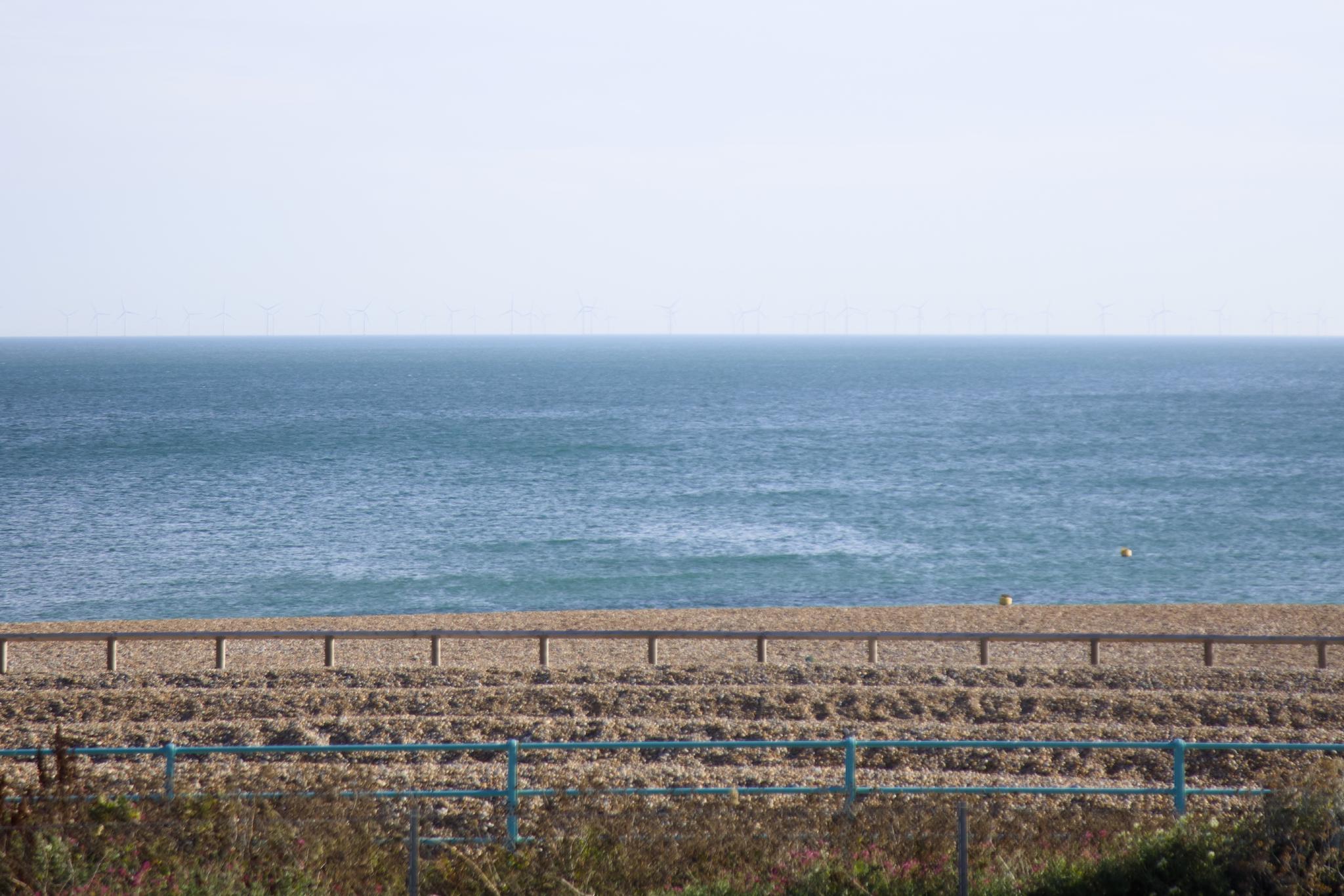 Offshore wind turbines on the horizon behind the shingle beach