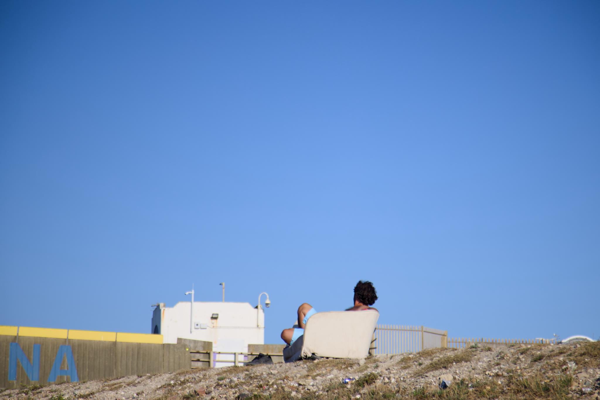 Man relaxing in an armchair on the shingle bank above the marina
