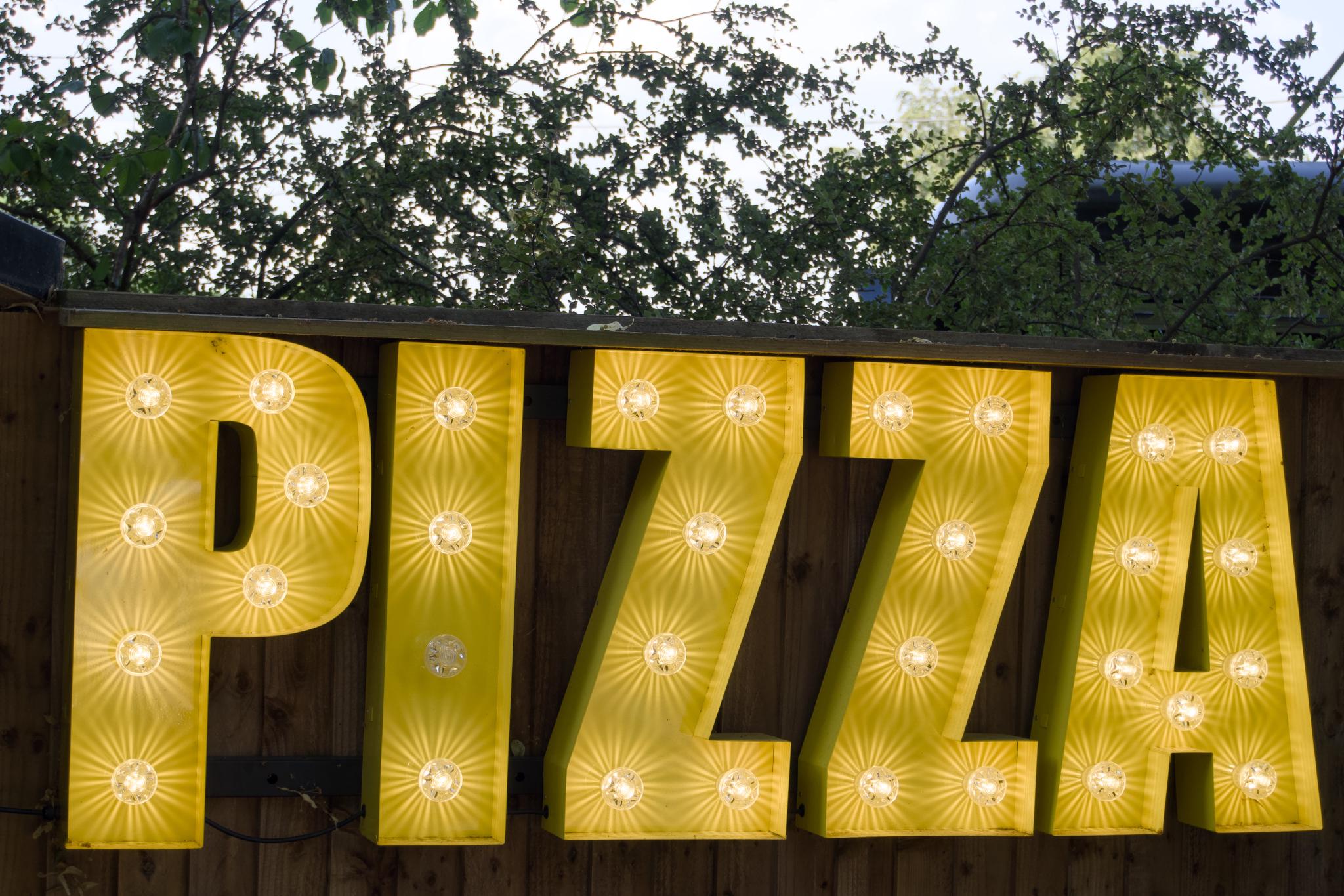 Yellow illuminated PIZZA sign on a wooden fence