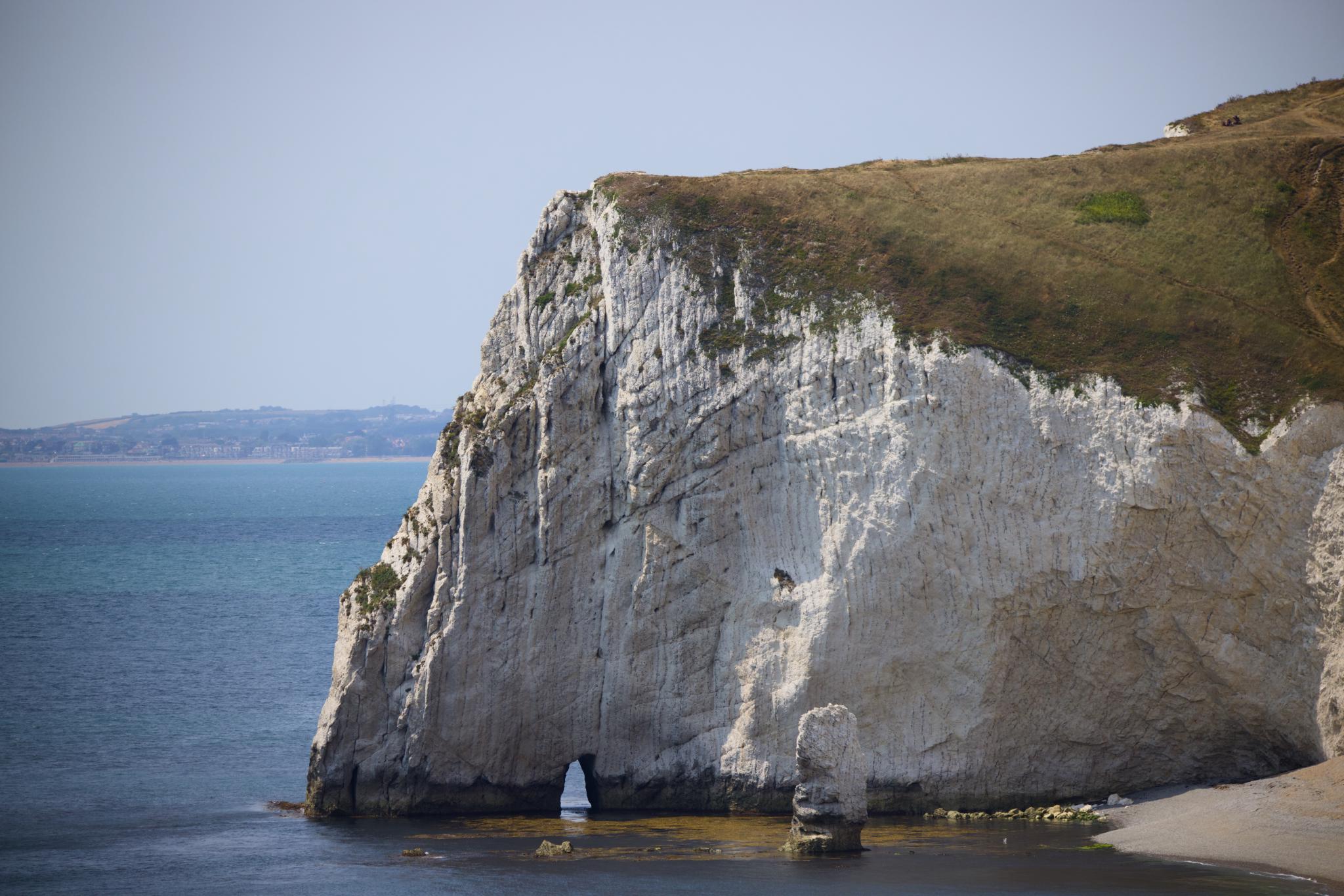 White chalk cliff with a small arch and a sea stack at its base