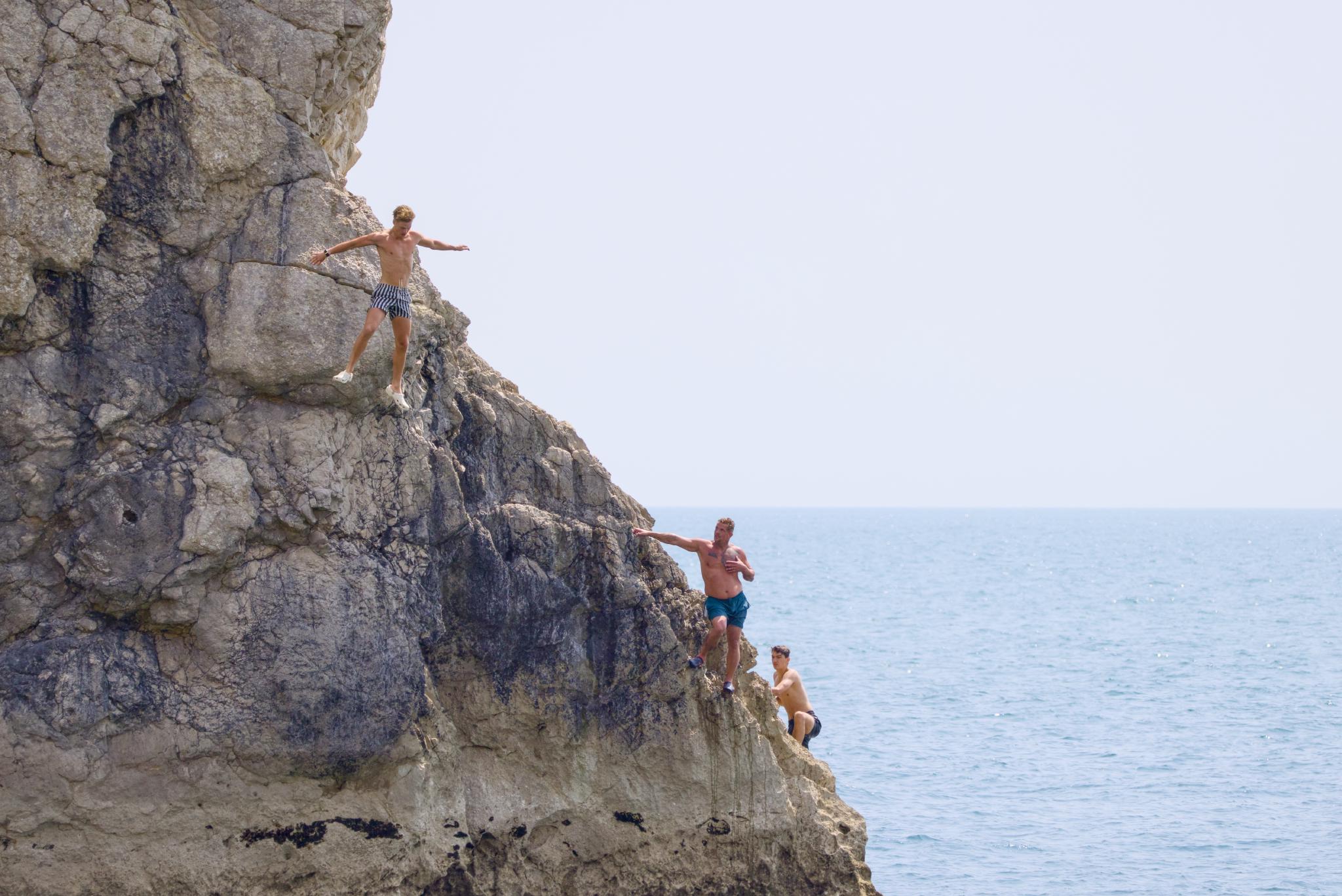 Three men climbing the rocks by the sea