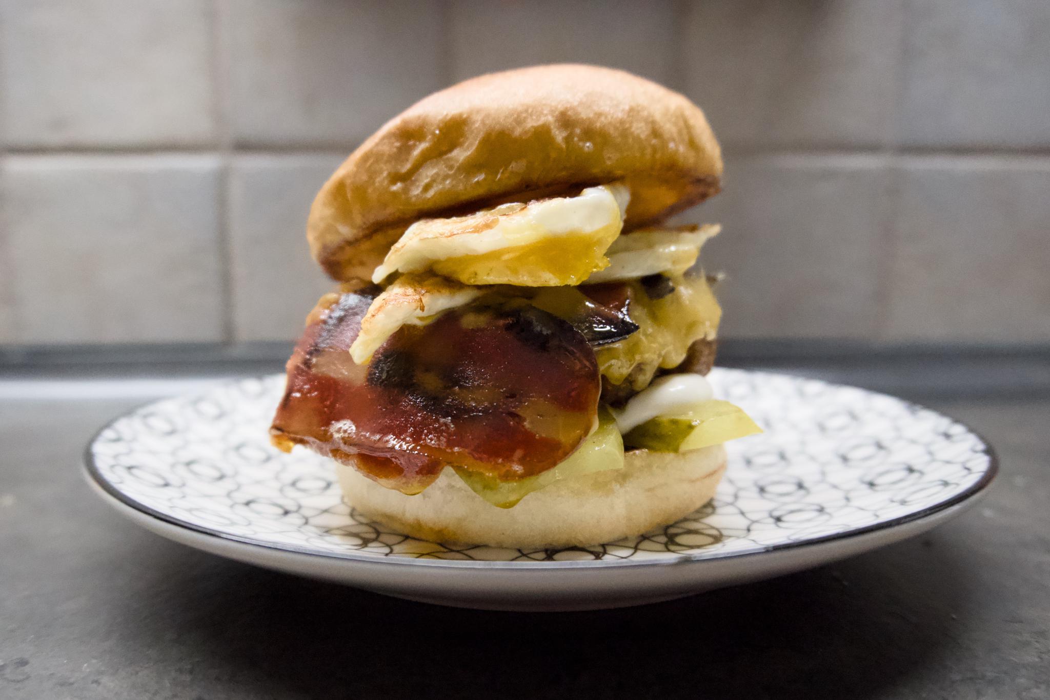 Burger with plant-based patty, fried egg, cheese, vegan bacon and pickles on a plate