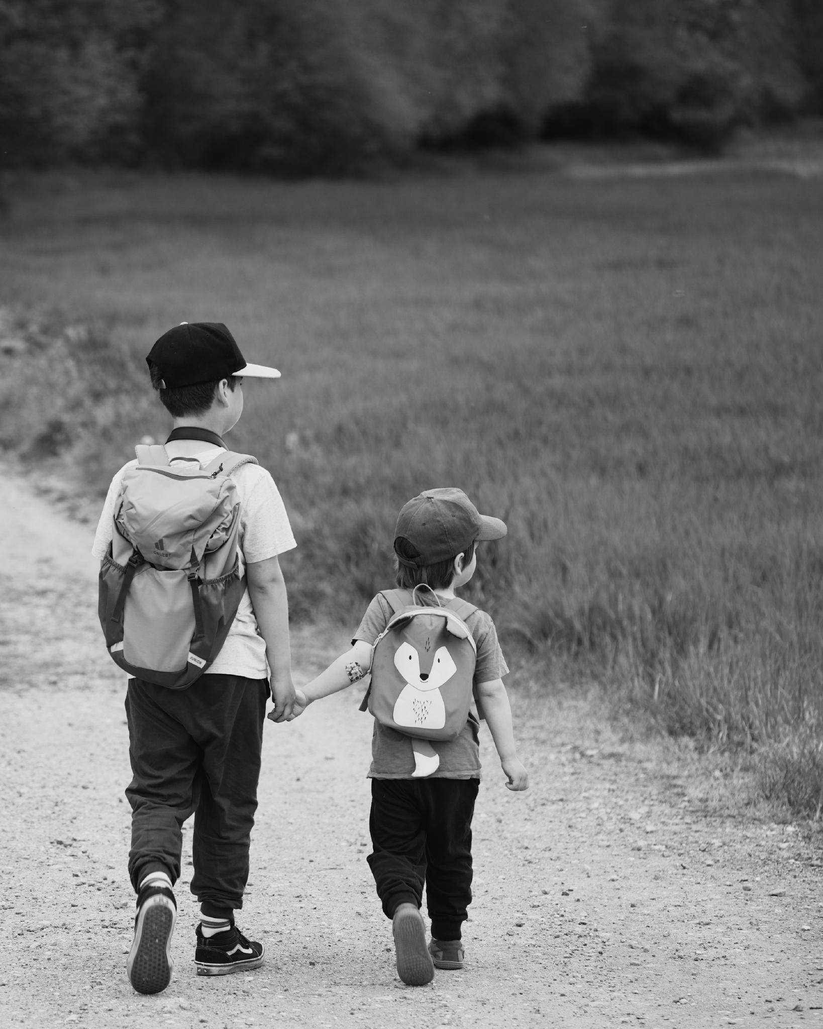 Black and white photo of two brothers walking hand in hand along a dirt path, green field beside them