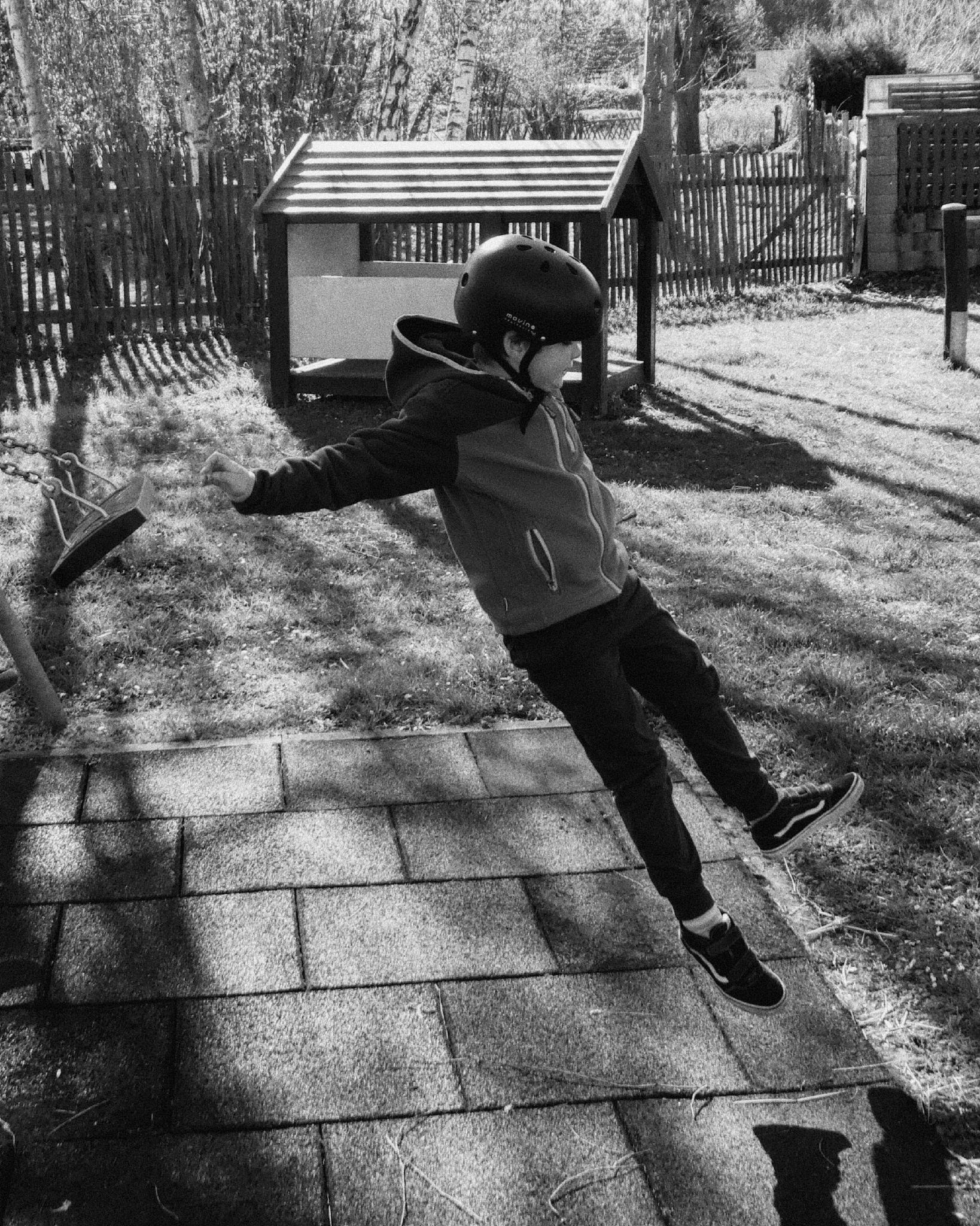 Black and white photo of a child mid-jump in a garden, wearing a helmet