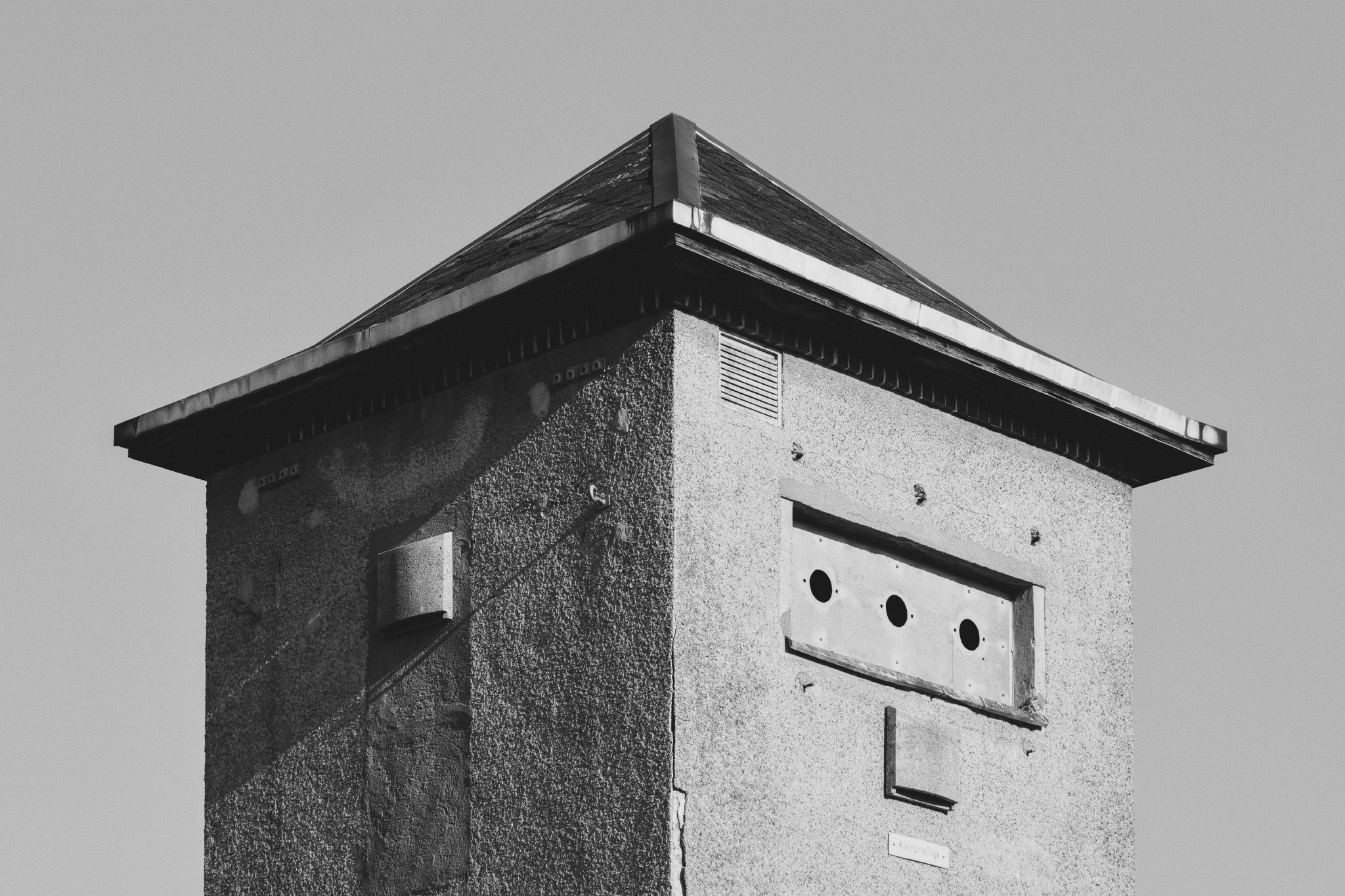 Top of a concrete utility tower against a grey sky, black and white