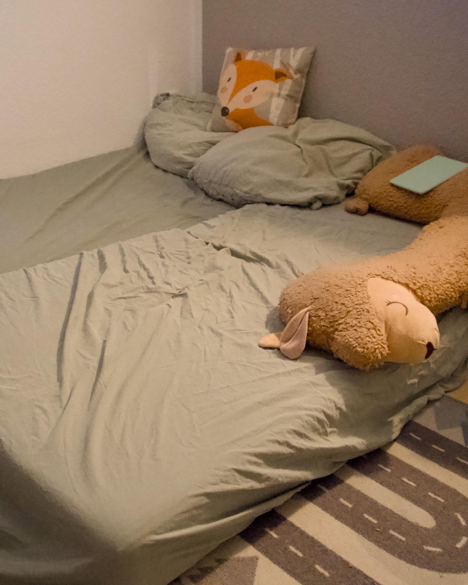 Makeshift floor bed in the playroom with a fox cushion and a sheep plush