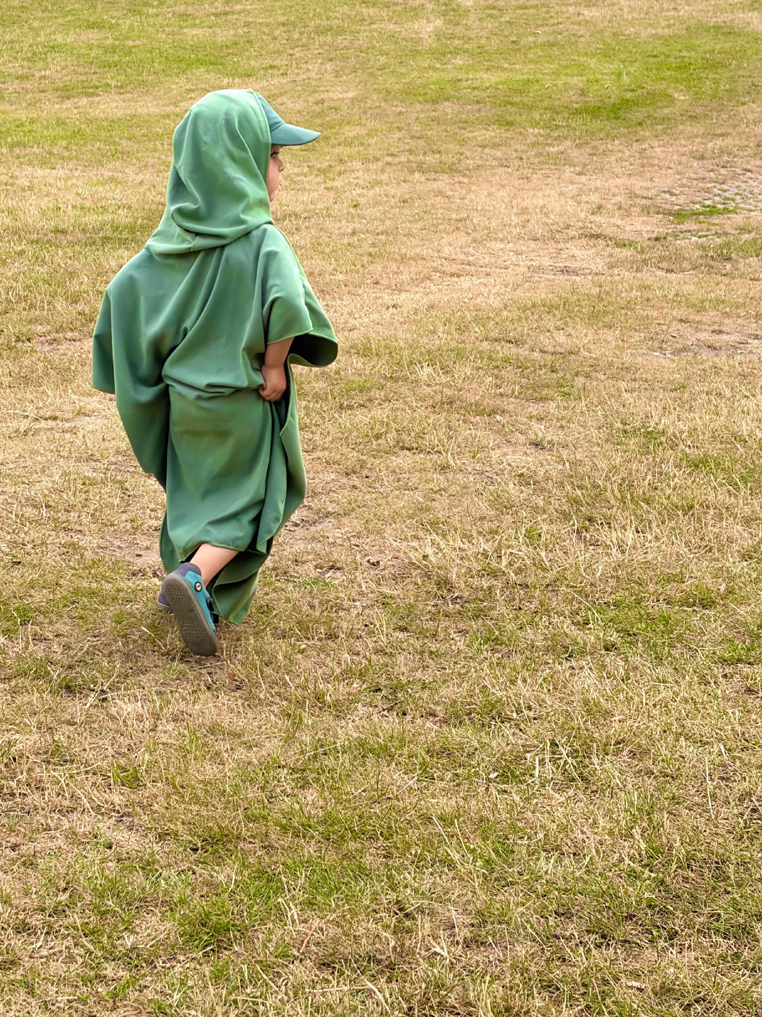 Child wrapped in a green hooded towel walking across grass