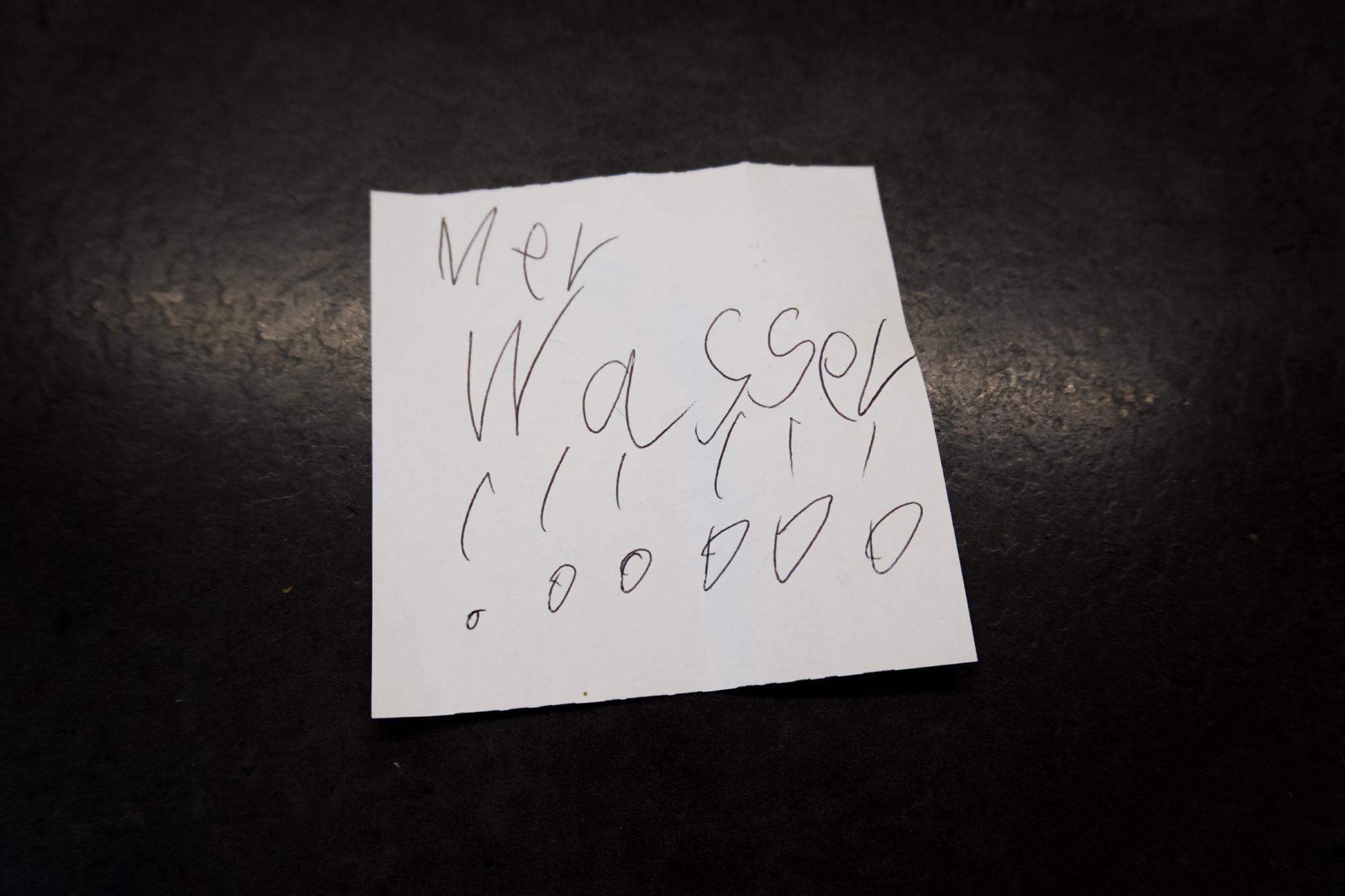 A small handwritten note on a dark surface reading 'Mer Wasser !!!' in a child's handwriting