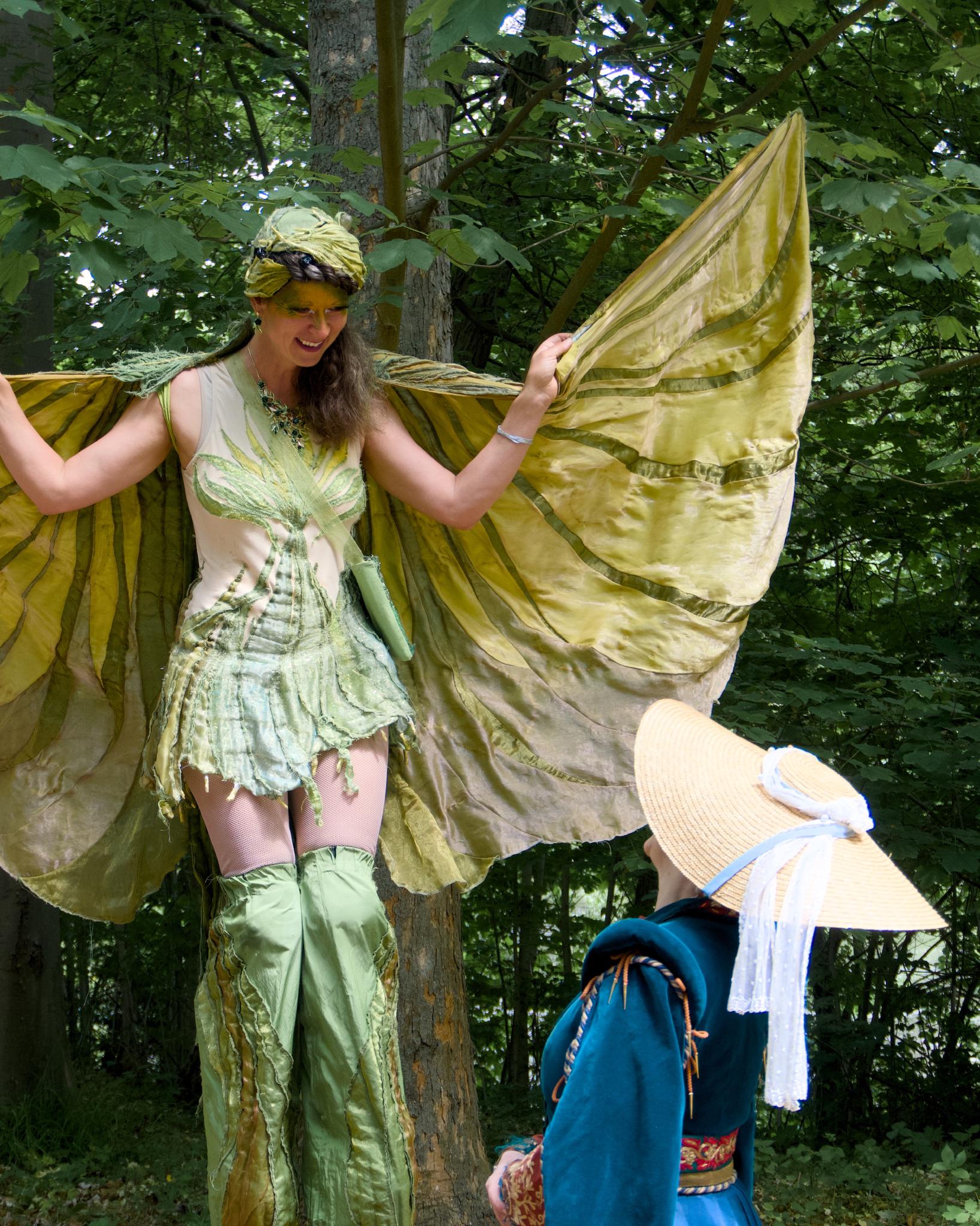 A performer on stilts in a green fairy costume